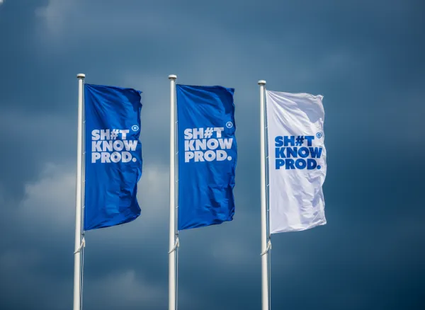 Apply logo to three vertical banners on tall white poles. The background is a bright, high-contrast sky with layered cumulus clouds and brilliant sunlight. Two banners are brand-colored, one is white. Realistic wind-blown ripples, deep fabric folds, professional event photography.