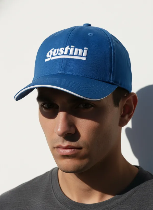 Apply the uploaded logo onto the front of a classic baseball cap worn by a man. The cap should use matching brand colors based on the logo. The scene features clean, minimalist lighting with sharp, dramatic shadows cast across the man's face and the white background wall. Photorealistic texture, medium close-up shot, professional fashion photography, 8k.