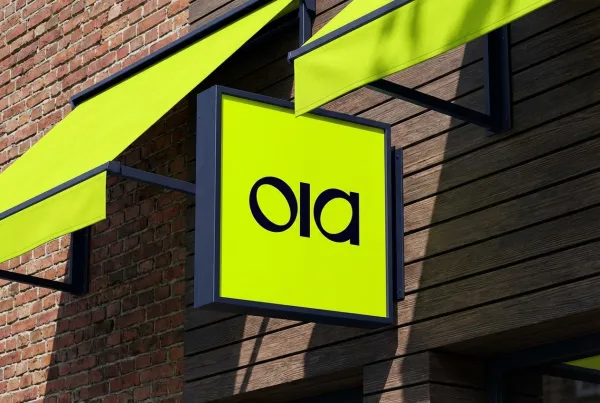 Apply the uploaded logo onto a square wall sign. The awning and frames should use matching brand colors. Background features a red brick wall and dark slatted surface with sharp diagonal sunlight shadows. Modern graphic style, medium shot from a slightly low angle, realistic textures, 8k.